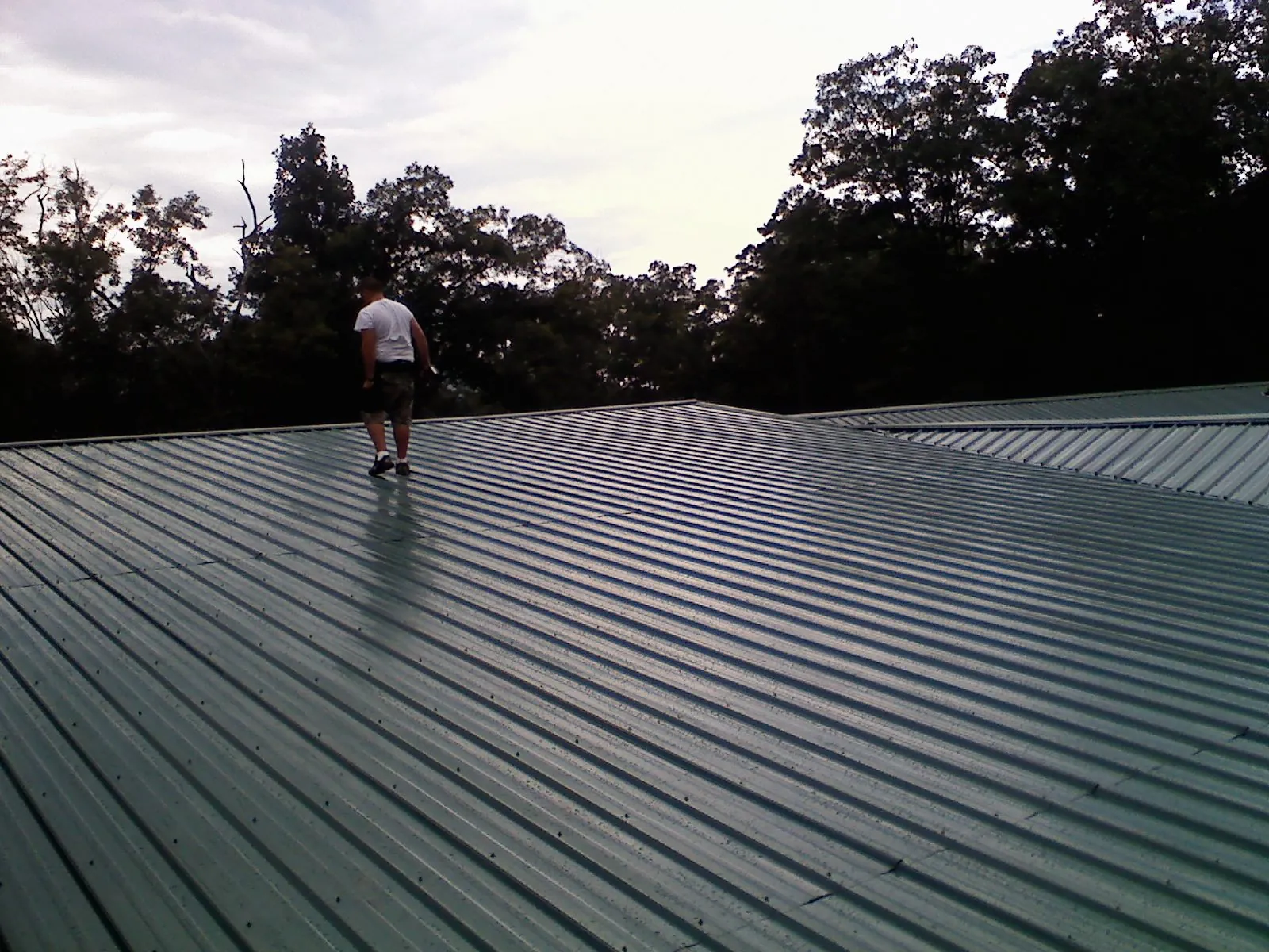 Roofer walking a wide expanse of new green metal roofing in De Soto