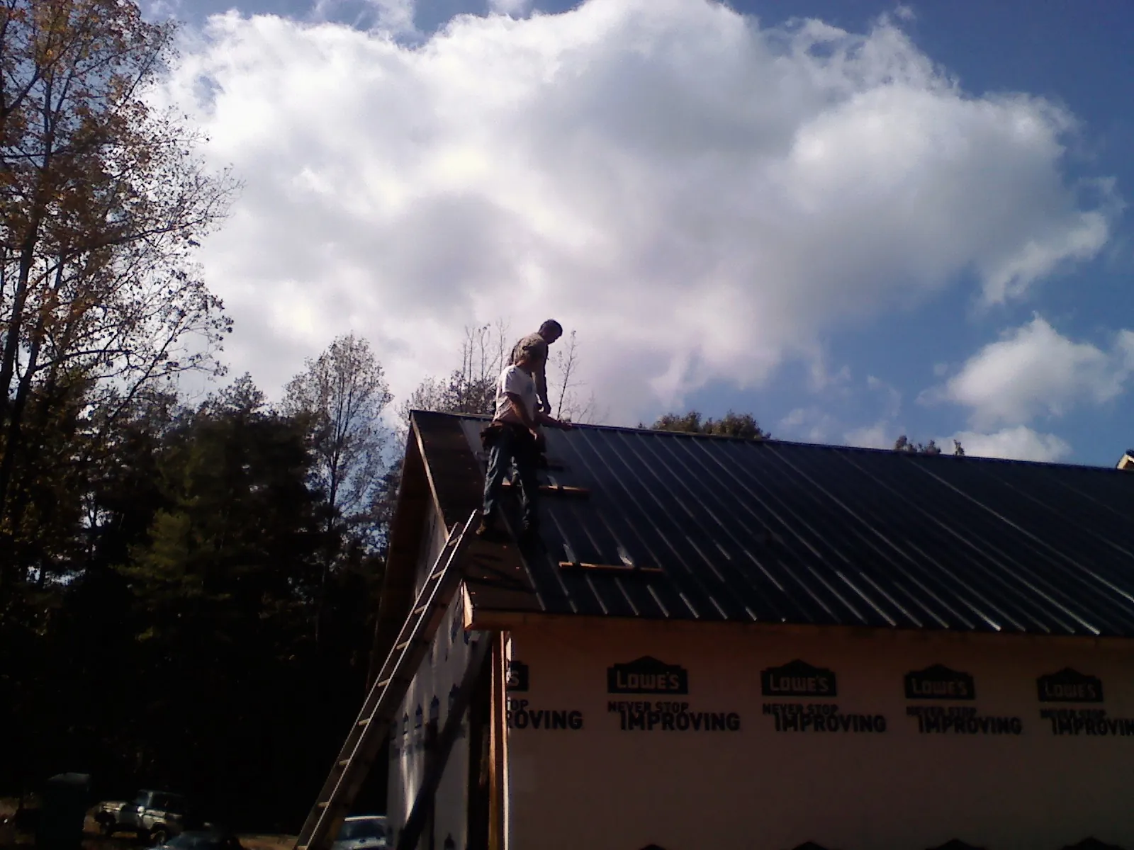 Roofer fastening dark metal panels high against a cloudy sky, from a Roof Inspection job in De Soto